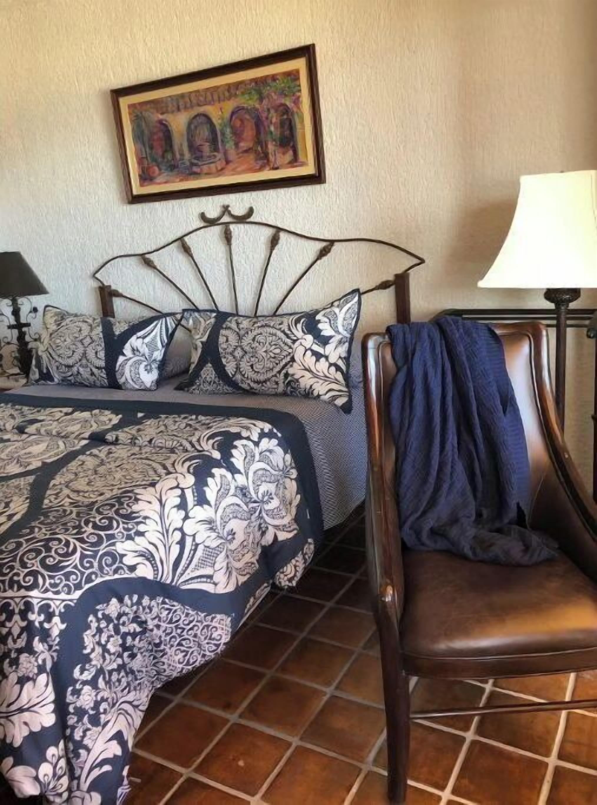 A bedroom with a bed, a chair, a lamp, and a painting on the wall.