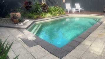 A rectangular swimming pool with clear water, surrounded by a tiled deck and potted plants.