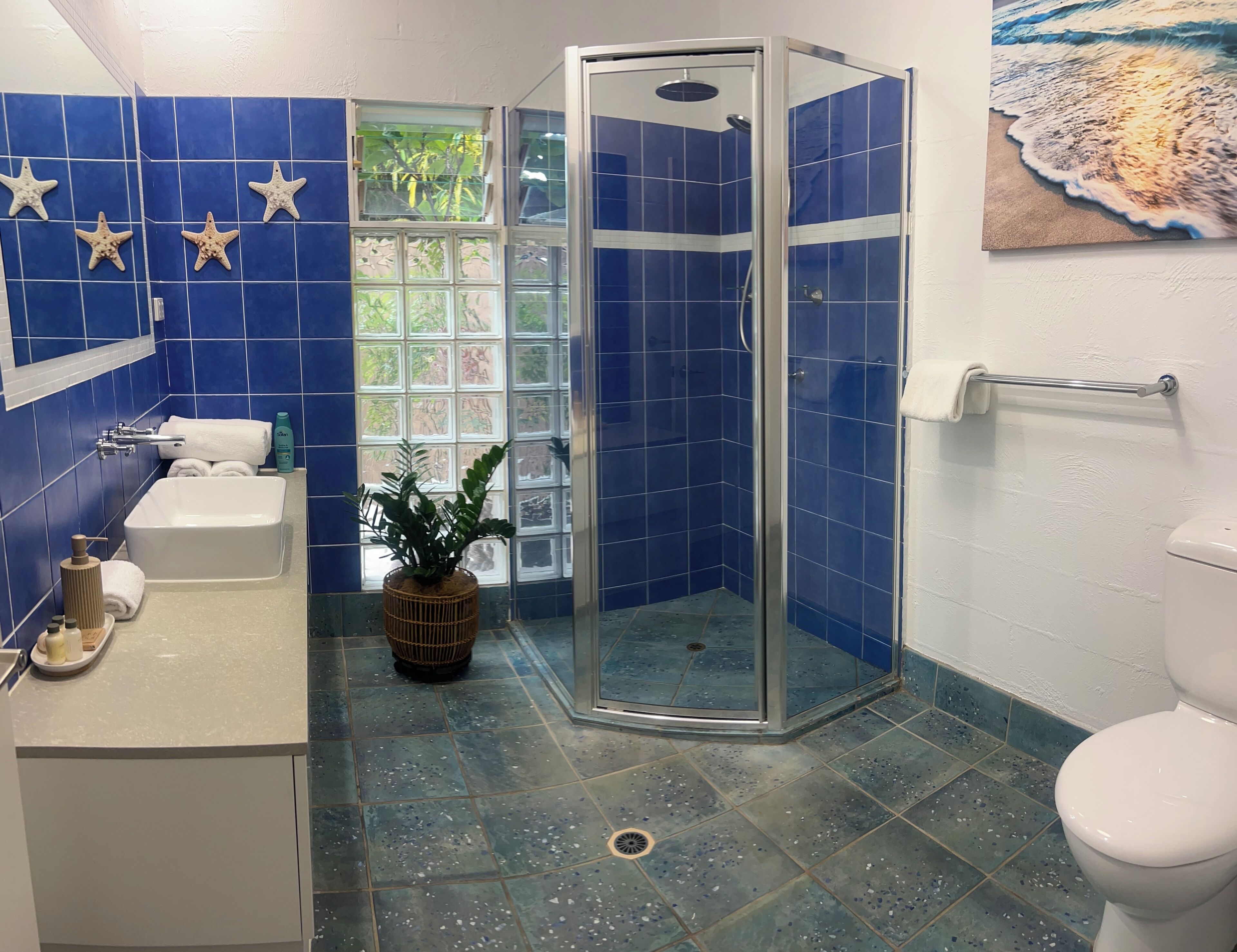 Une salle de bain avec des carreaux bleus, une douche, un lavabo et une fenêtre donnant sur un beau paysage.