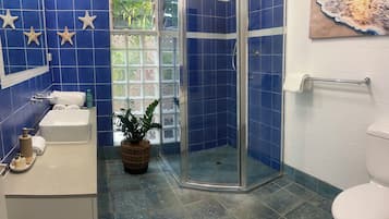 A bathroom with blue tiles, a shower, a sink, and a window with a view.