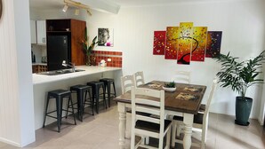 A modern kitchen with a built-in refrigerator, bar stools, a dining table with chairs, and a potted plant. -  Murriyan A Tropical Villa (Port Douglas)