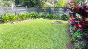 A well-maintained grassy area with a wooden fence, surrounded by various plants and shrubs. -  Murriyan A Tropical Villa (Port Douglas)