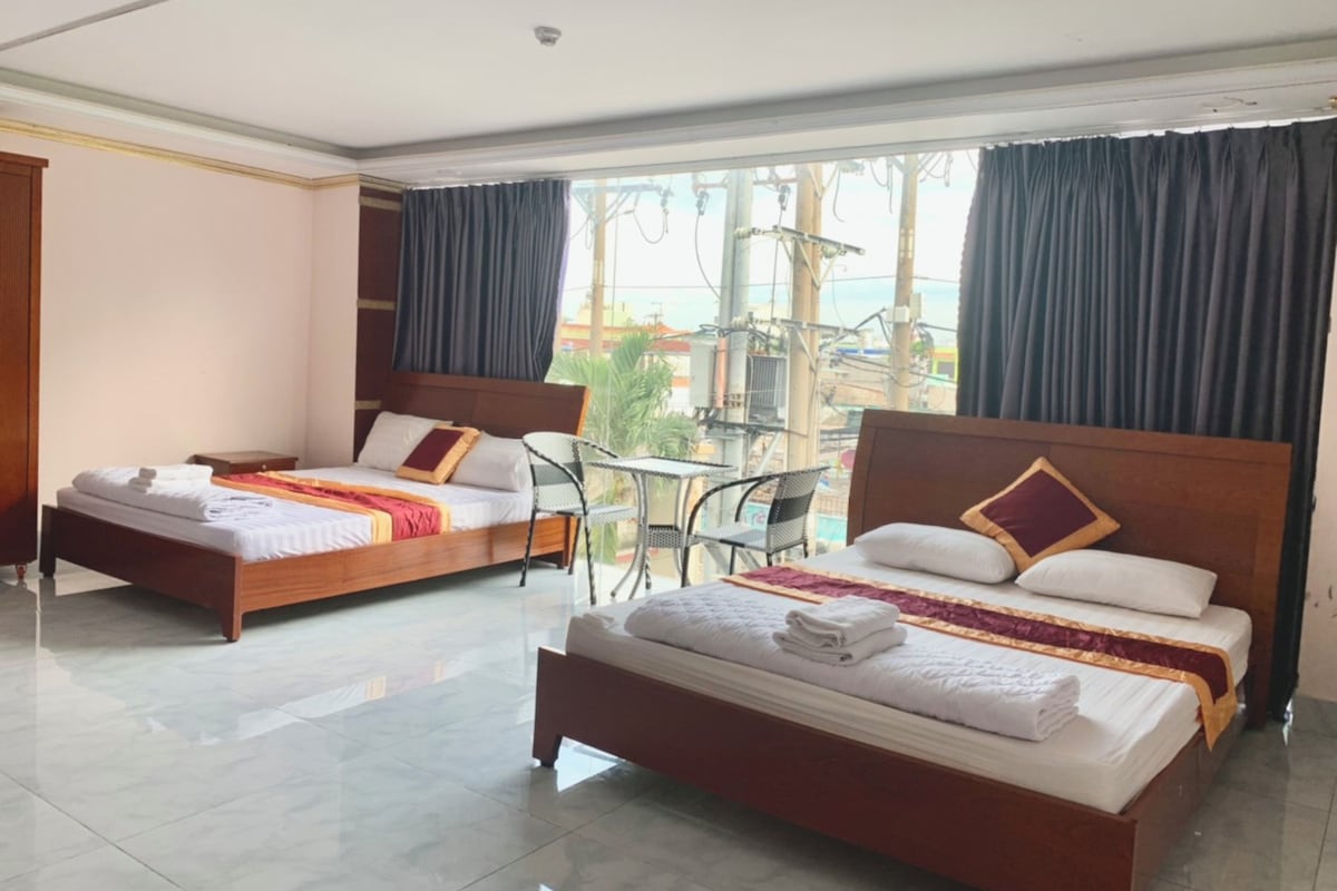 A hotel room with two beds, a balcony with a table and chairs, and a view of the cityscape.