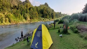 A tent set up near a river with a forested hillside in the background. - Potrobayan River Camp (Pundong)