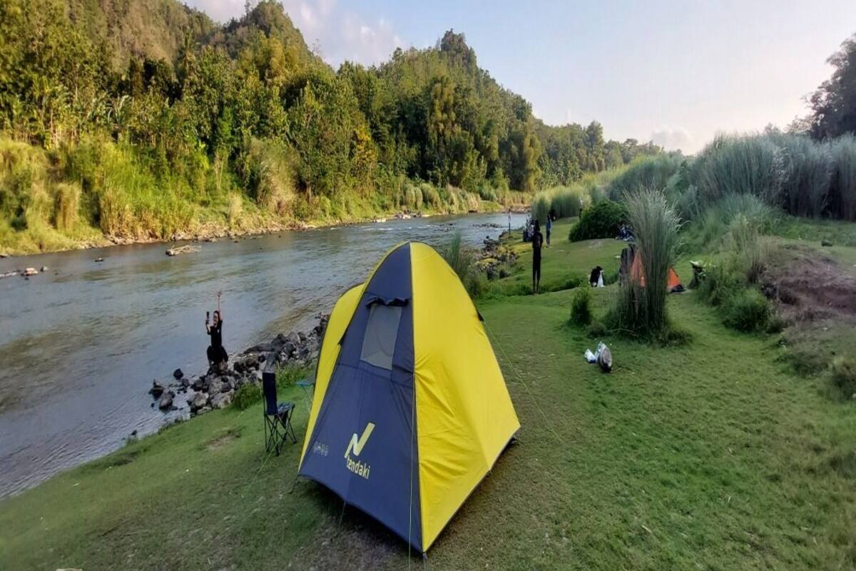 A tent set up near a river with a forested hillside in the background.