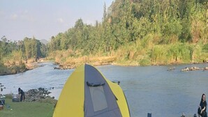 A yellow and gray tent with a logo, set up near a river with a chair and a table nearby. - Potrobayan River Camp (Pundong)