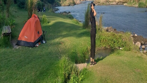 A tent set up on a grassy area near a river, with a person standing nearby. - Potrobayan River Camp (Pundong)