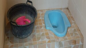 A small bathroom with a blue toilet and a black bucket with a pink scoop. - Potrobayan River Camp (Pundong)