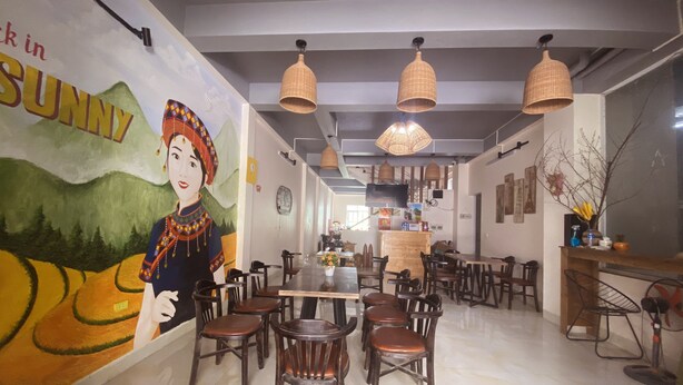 A restaurant interior with a mural, wooden tables, and hanging pendant lights. - Sunny Bao Lac Homestay (Bao Lac)