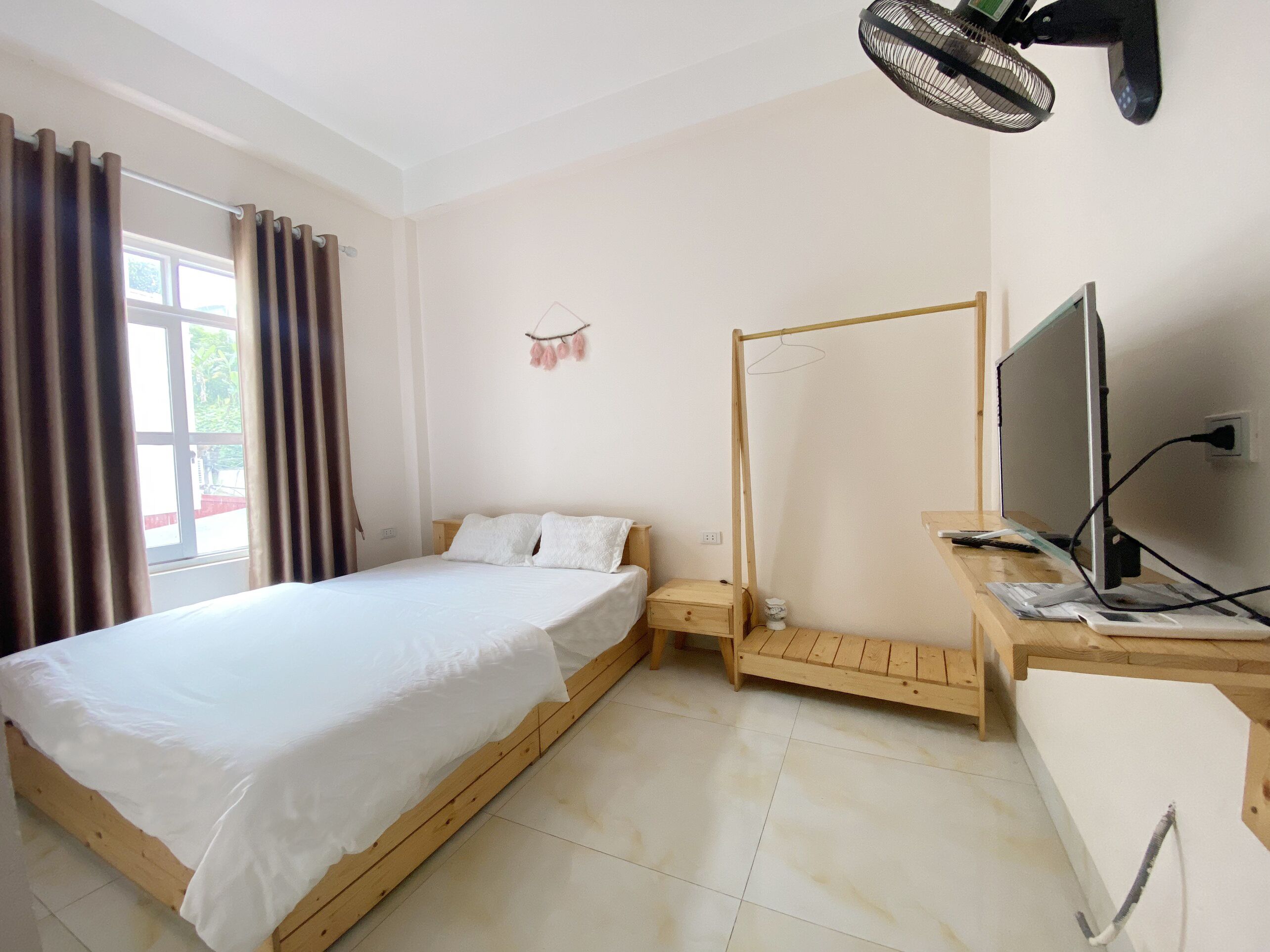 A bedroom with a bed, a TV, a fan, and a window with curtains.