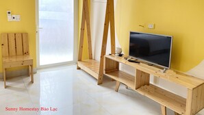 A bright room with yellow walls, a wooden bench, a TV on a wooden stand, and a door leading outside. - Sunny Bao Lac Homestay (Bao Lac)