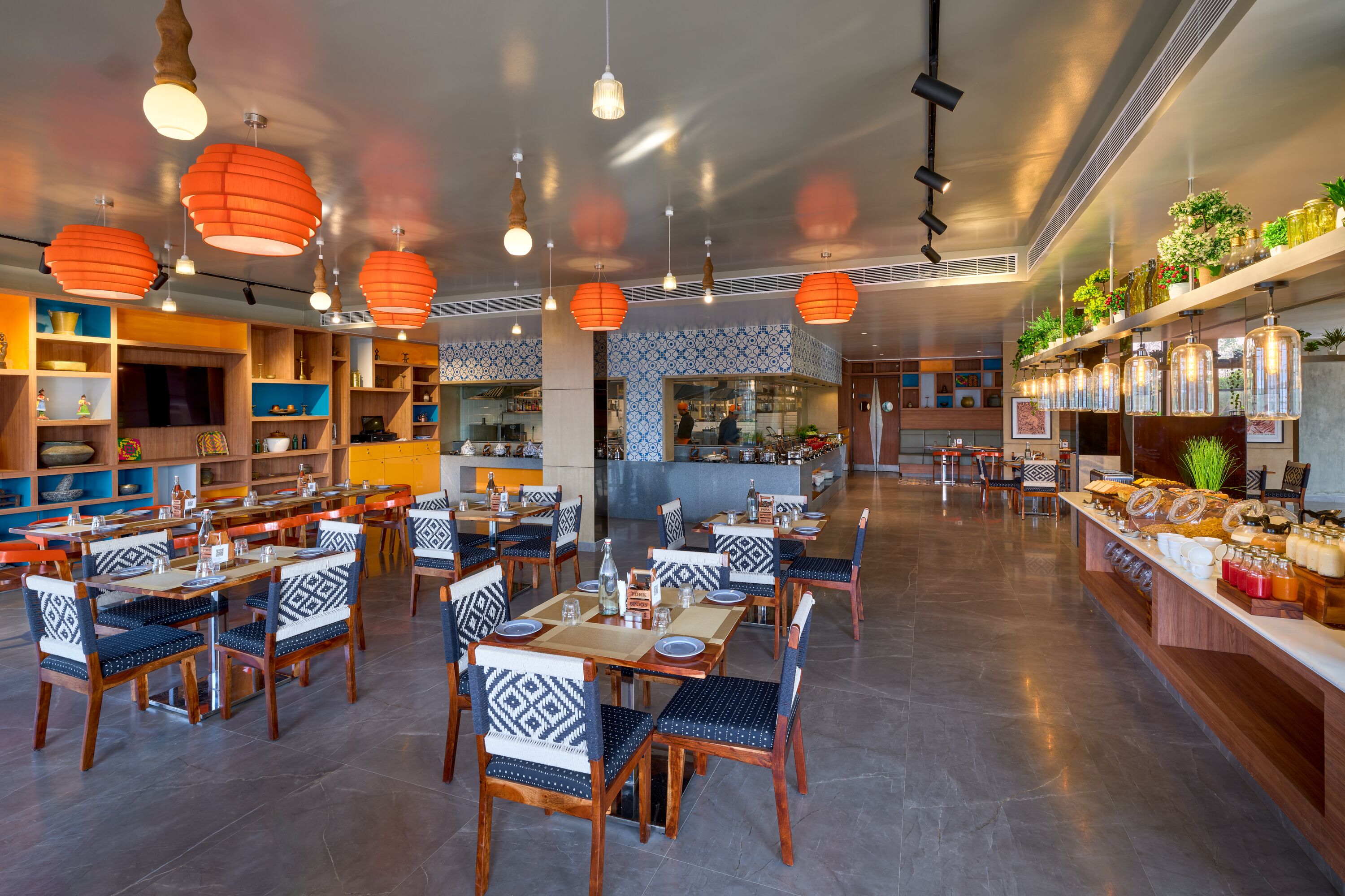 Un restaurante con varias mesas y sillas, una zona de cocina y estantes con distintos artículos.