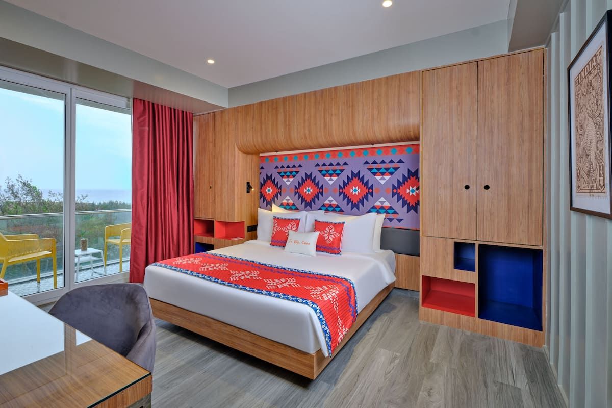 Ett modernt hotellrum med en stor säng, ett träpanelat sänggavel och utsikt över havet genom stora fönster.