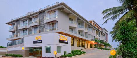 A multi-story hotel with a modern design, featuring balconies, a well-lit entrance, and a parking sign.
