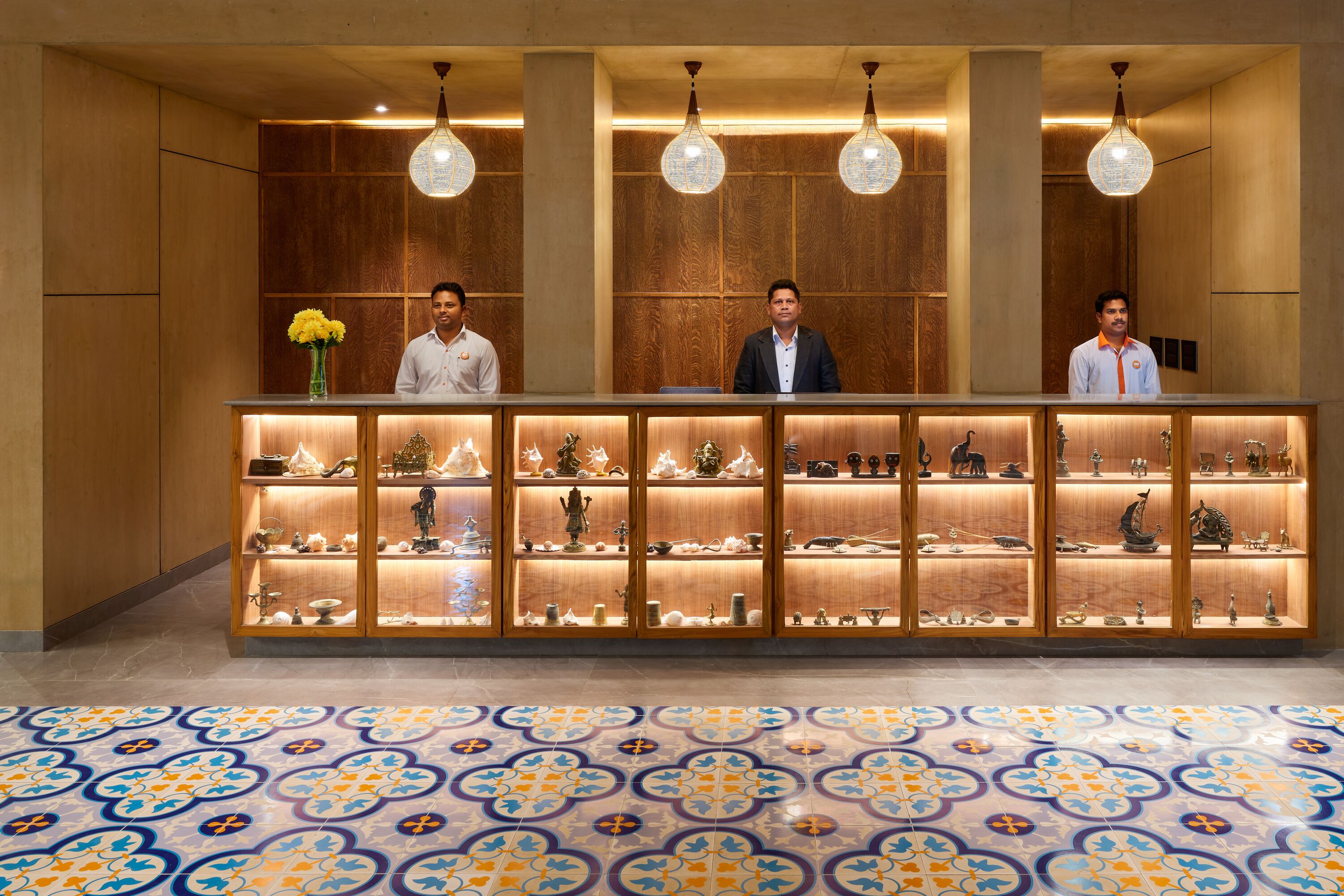 A reception area with a wooden reception desk, three staff members, and a patterned floor.