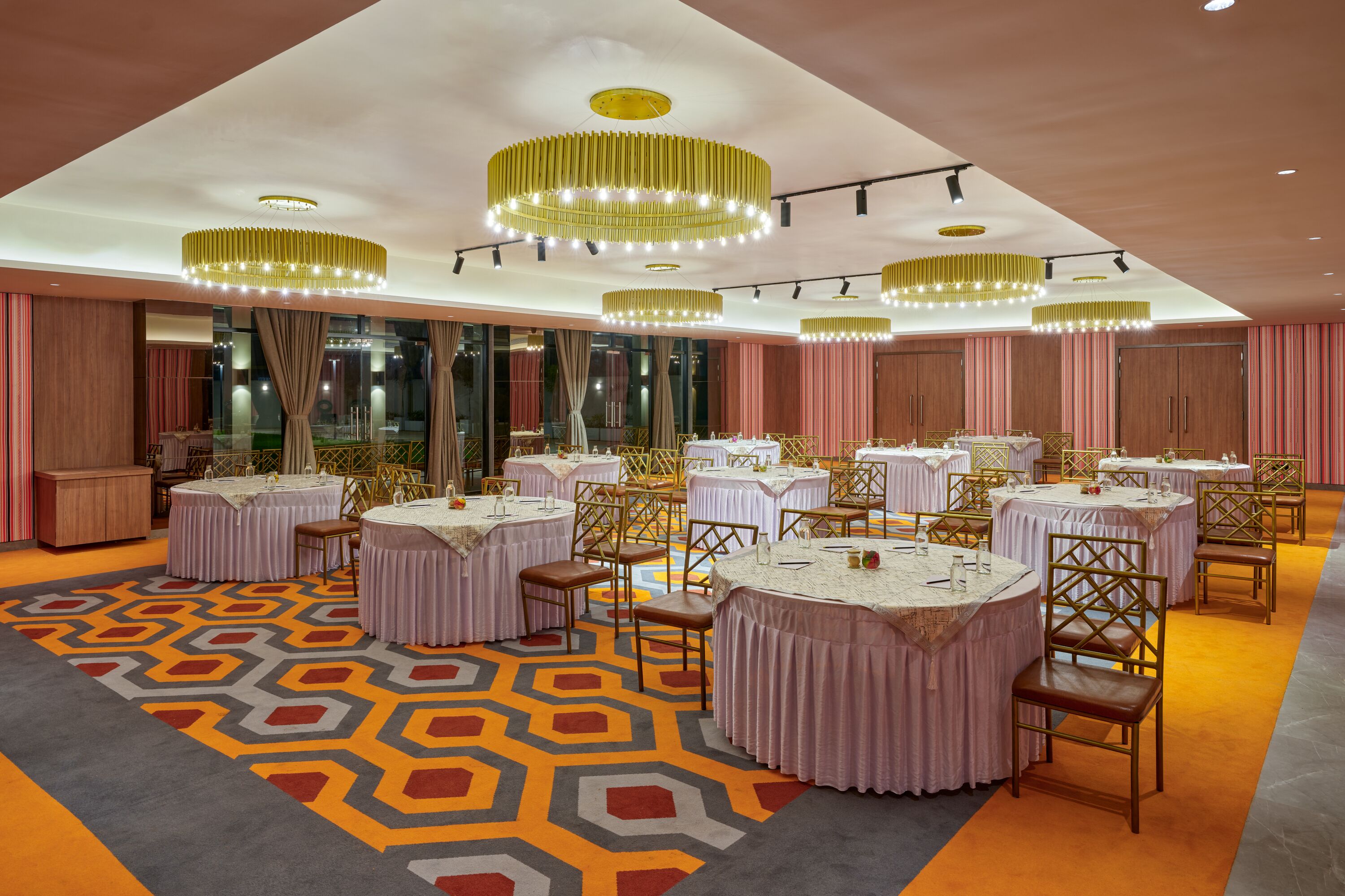 A banquet hall with round tables, chandeliers, and a patterned carpet.