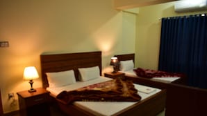 Habitación de hotel con una cama, una mesita de noche con lámpara y una ventana con cortinas.
