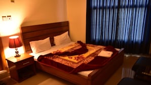 Una cama bien hecha con un edredón estampado, una lámpara de noche y un cabecero de madera.