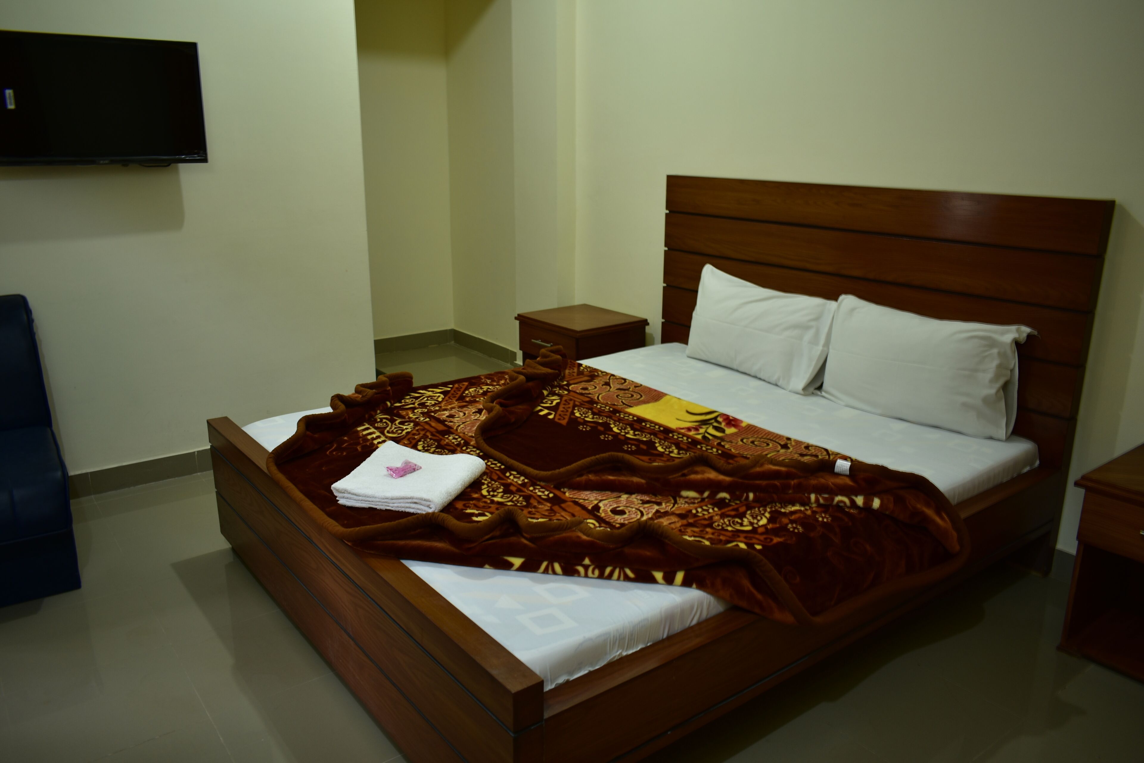 A wooden bed with a patterned blanket, white pillows, and a small bedside table.