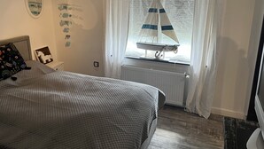 Et soveværelse med seng, et vindue med gardiner, en radiator og vægdekorationer.