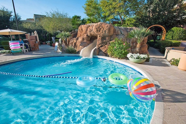 A swimming pool with a slide, inflatable rings, and a rock formation in the background.