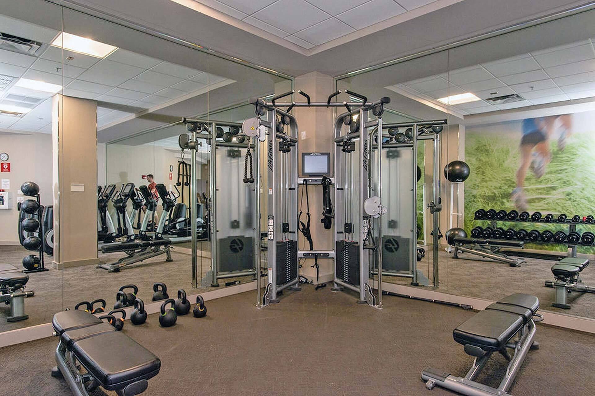 Et fitnesscenter med forskellig træningsudstyr, herunder løbebånd, styrkemaskiner og håndvægte.