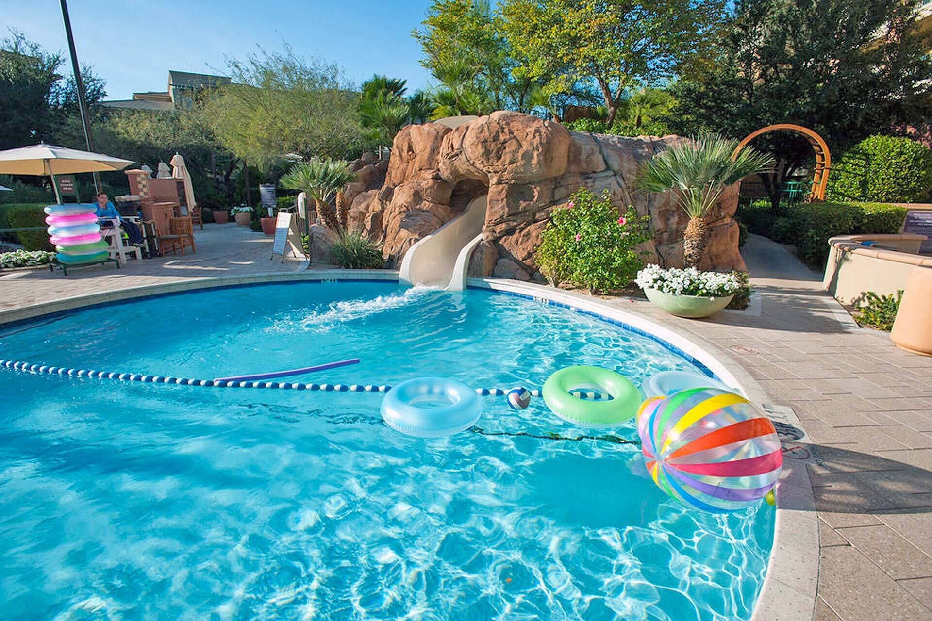 A swimming pool with a slide, inflatable rings, and a rock formation in the background.