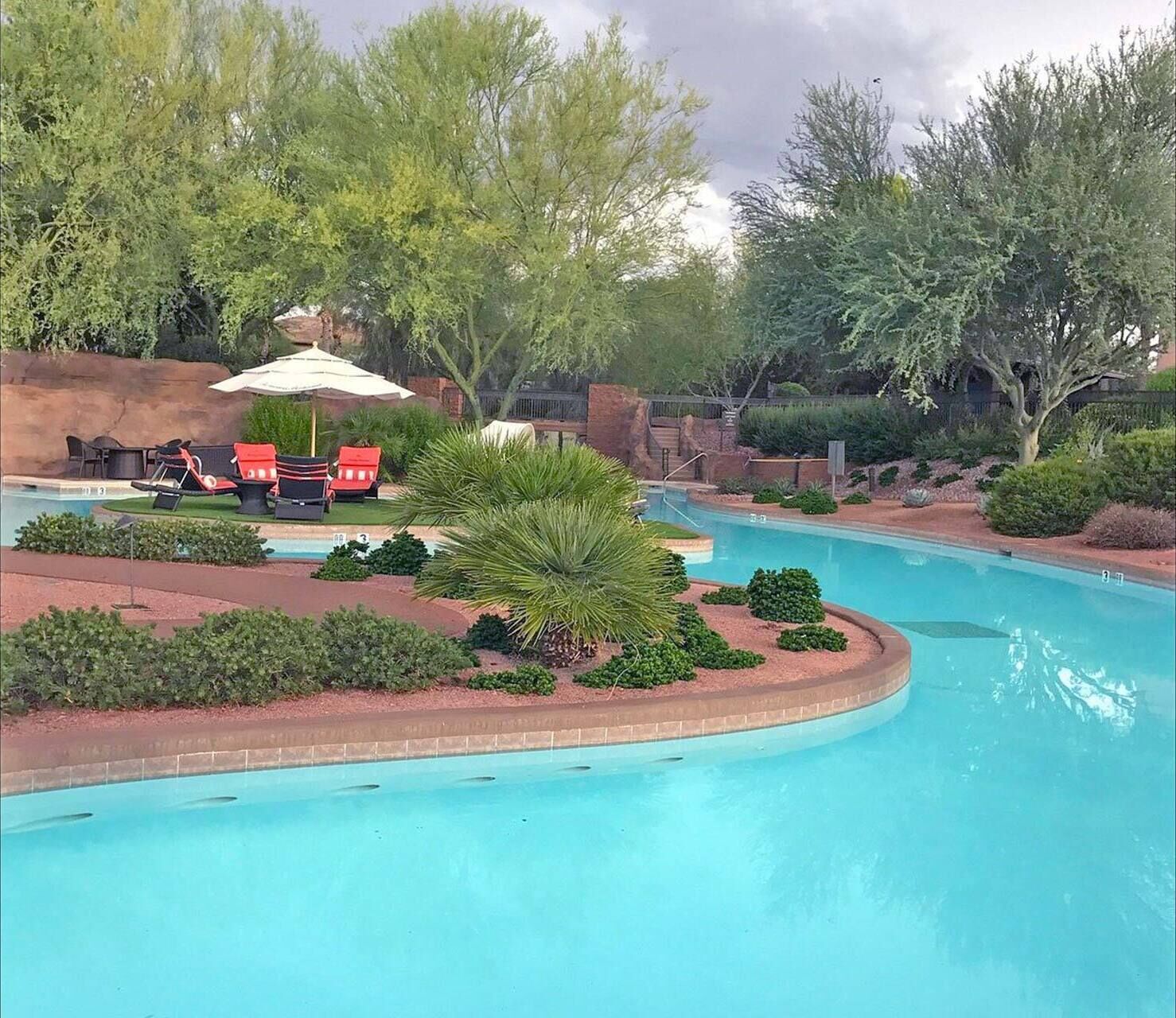 A swimming pool with lounge chairs and umbrellas, surrounded by landscaped greenery and trees.