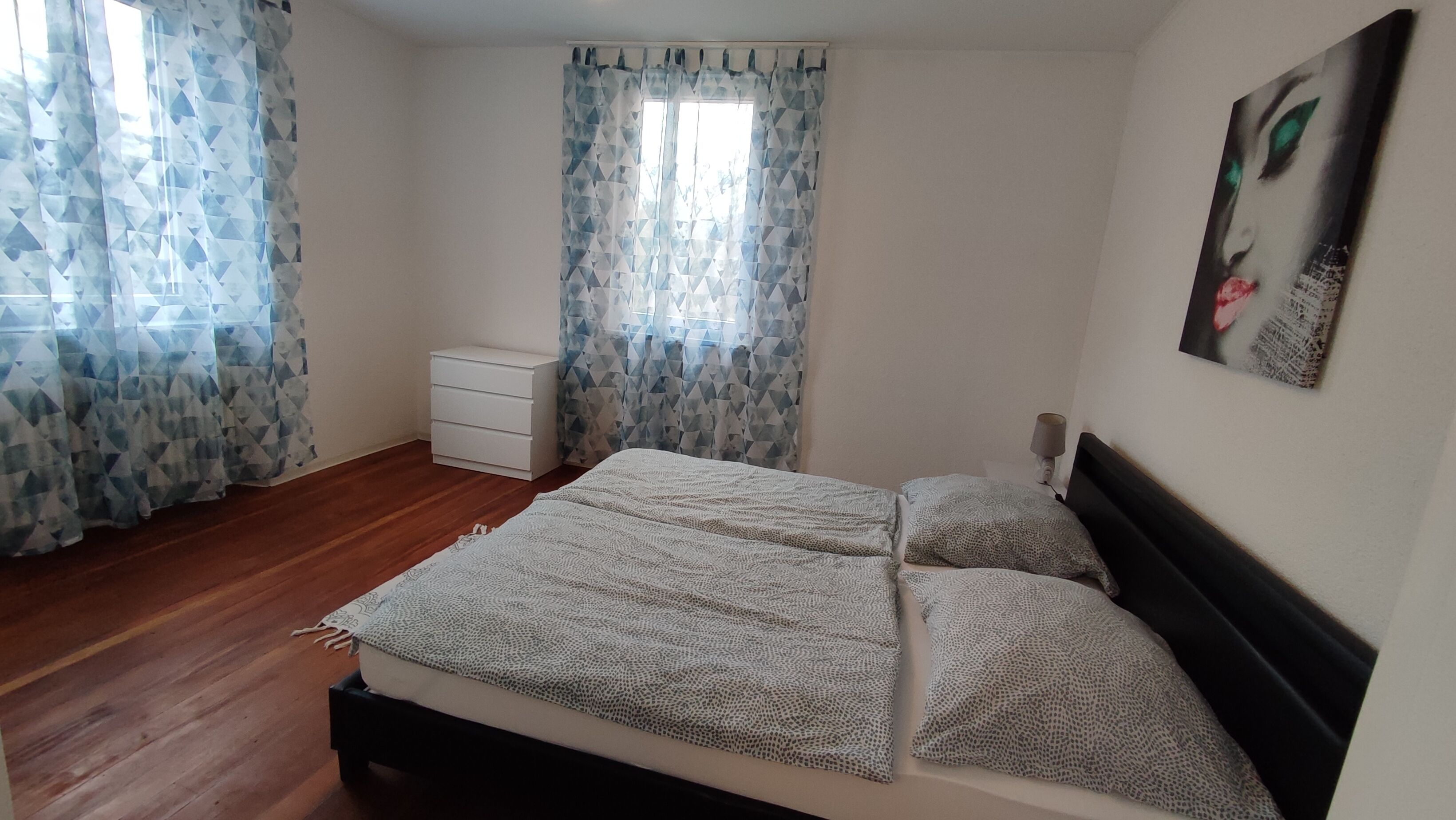 Ein Schlafzimmer mit einem Bett, einem Nachttisch, einer Kommode und einem Bild an der Wand.