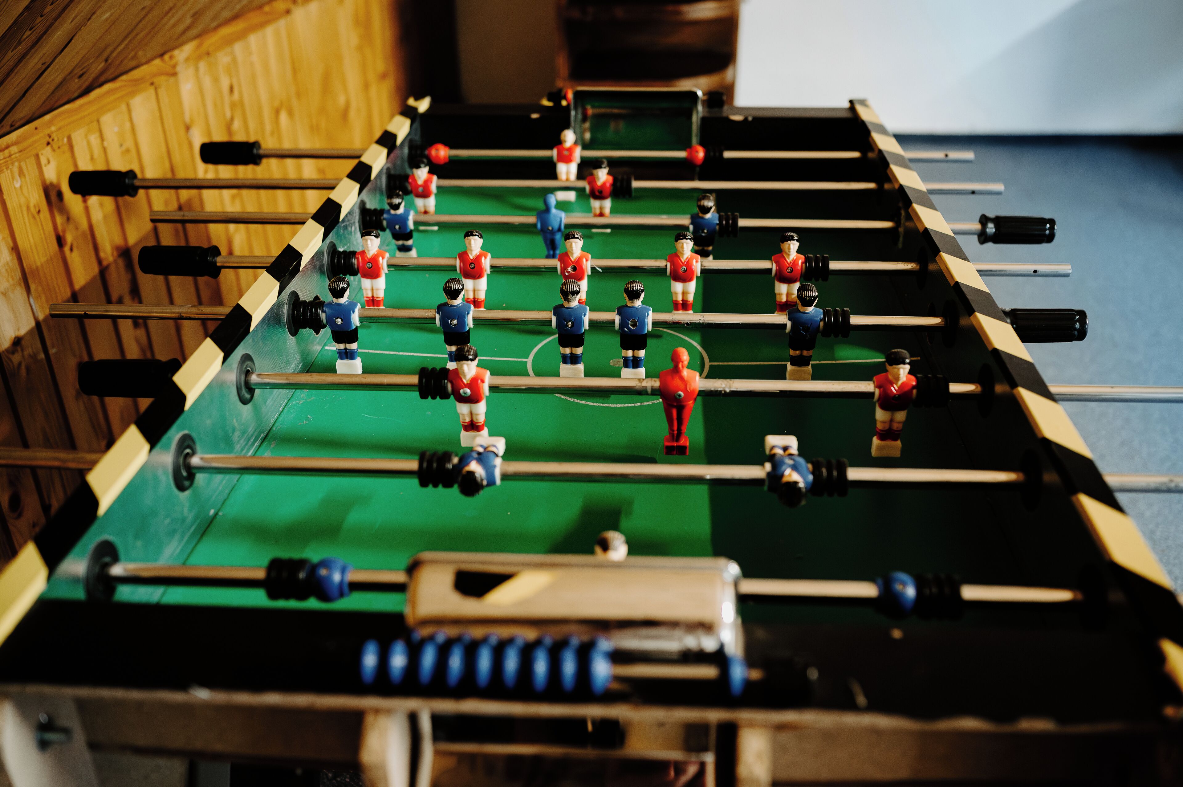 Una mesa de fútbolín con varios jugadores uniformados en rojo y azul.