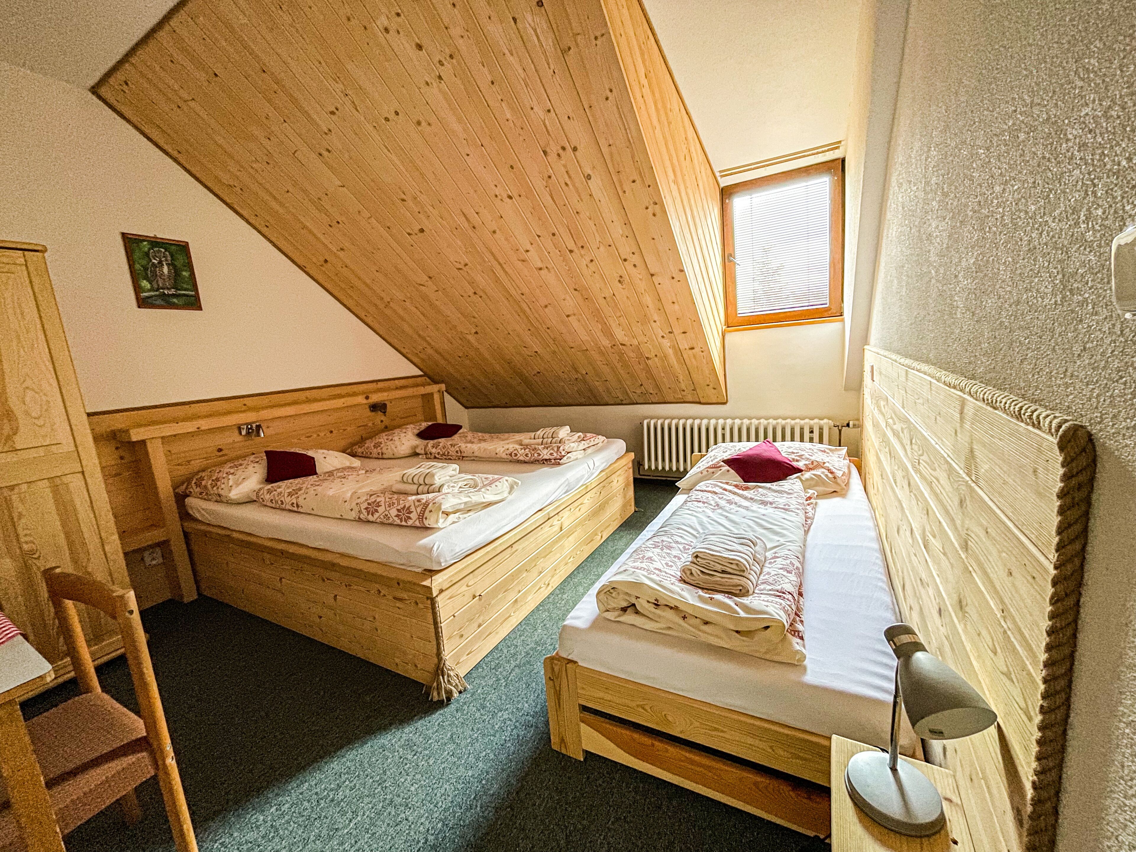 A small, cozy room with two wooden beds, a chair, a desk, and a window.
