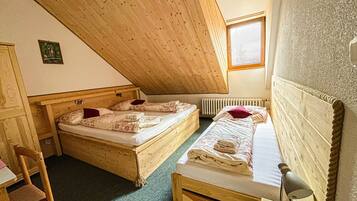 A small, cozy room with two wooden beds, a chair, a desk, and a window.