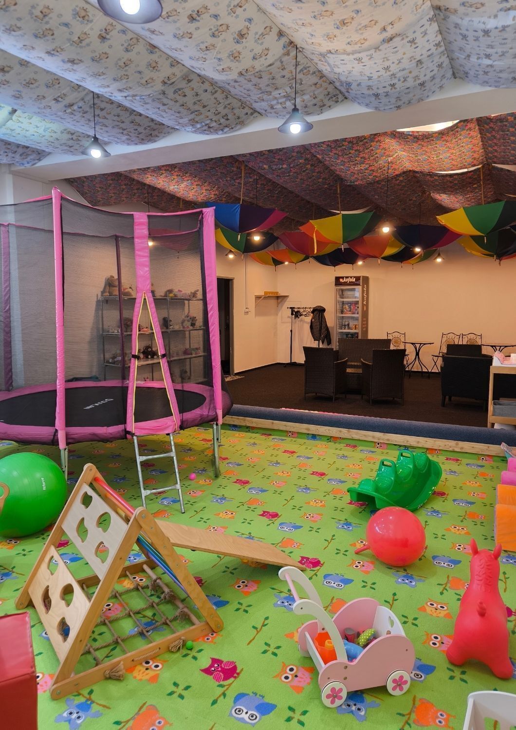 A playroom with a trampoline, climbing net, and various toys.