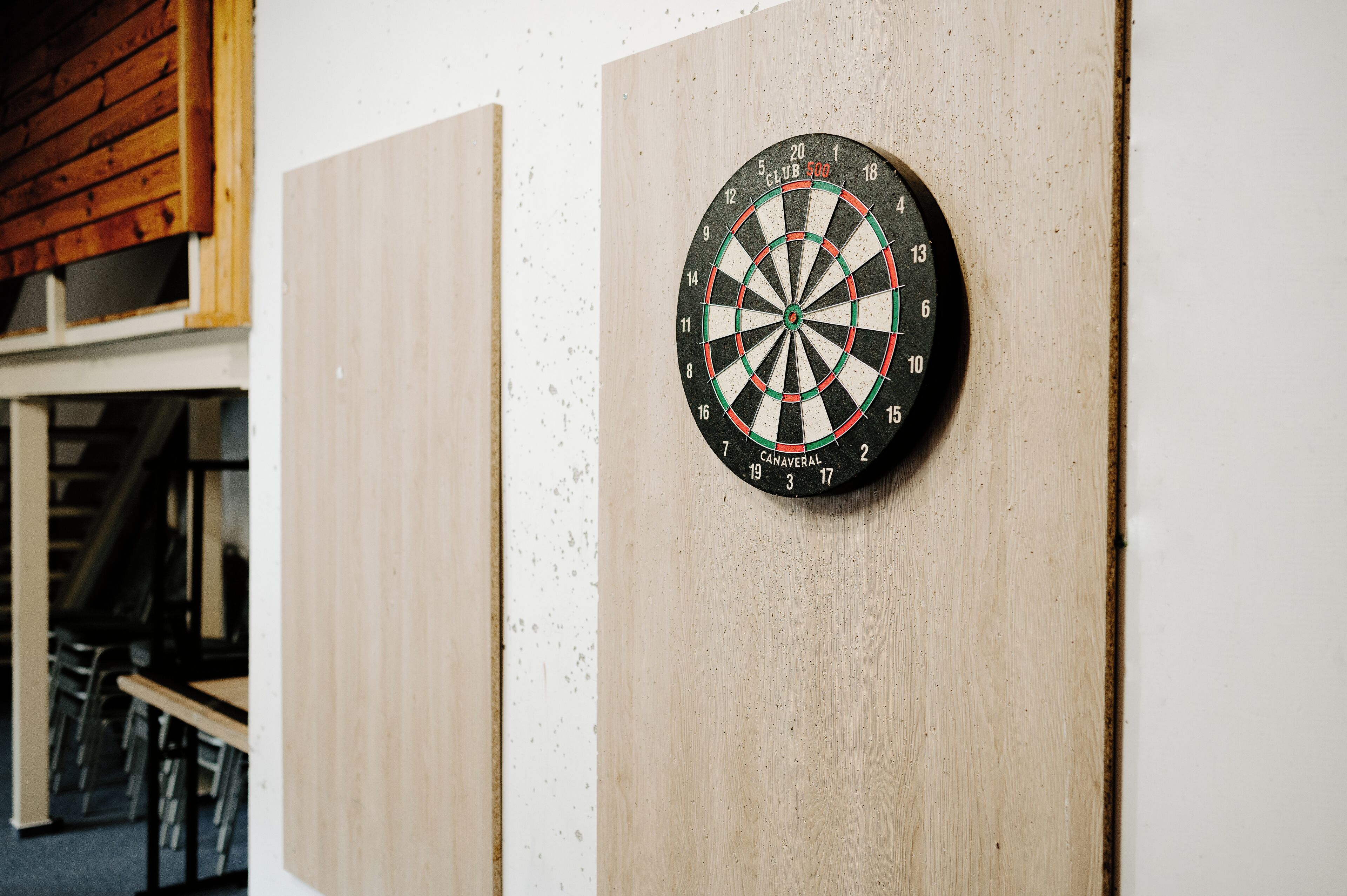 Een dartbord bevestigd aan een houten wand in een kamer met een trap en een houten plafond.