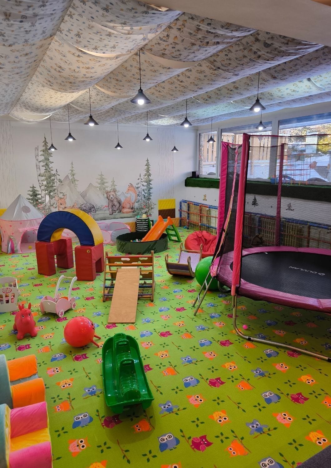 Une salle de jeux pour enfants avec un sol coloré, des structures de jeu et un trampoline.