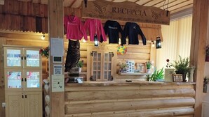 A wooden reception desk with a sign reading "RECEPCIA". There are two black shirts hanging above the desk. - Hotel Sova Ždiar (Zdiar)