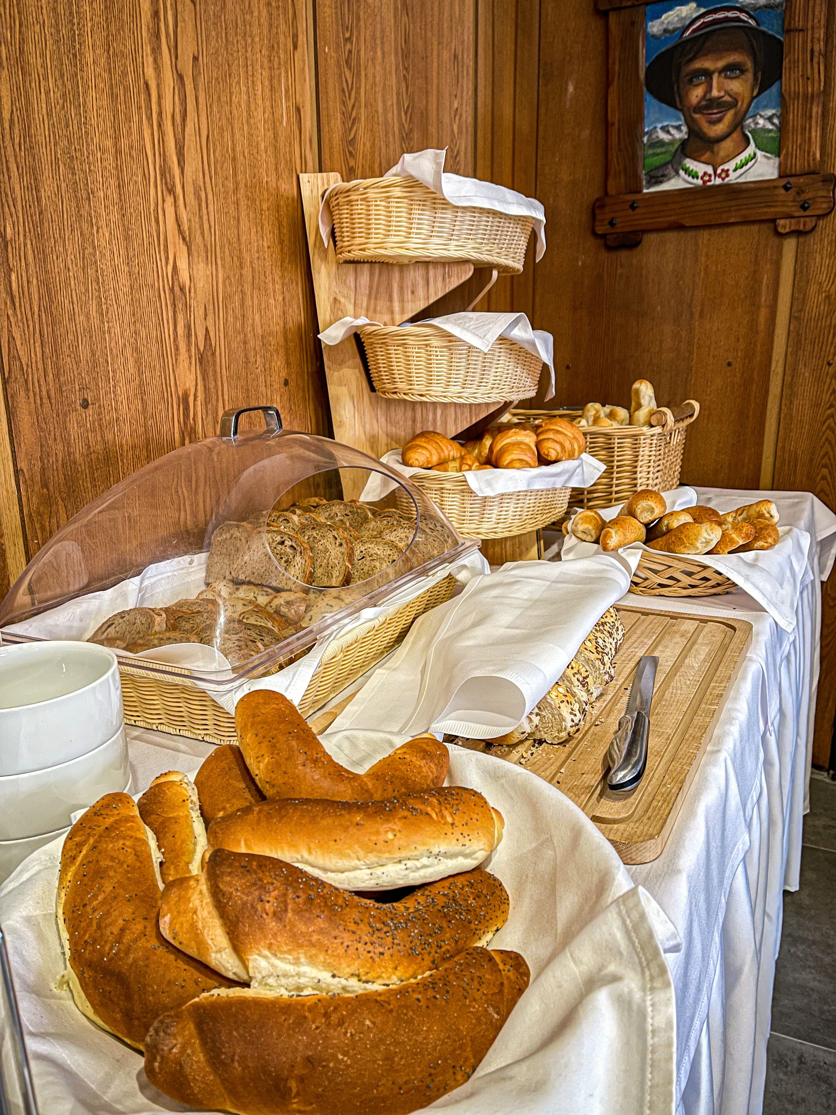 A breakfast buffet with various breads, pastries, and a knife on a wooden table.