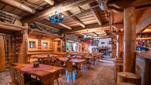 A rustic wooden interior with multiple wooden tables and chairs, a fireplace, and a variety of wooden beams and logs on the walls. - Hotel Sova Ždiar (Zdiar)