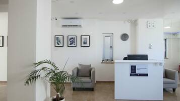 A reception area with a reception desk, a potted plant, a grey sofa, and framed pictures on the wall.