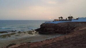 A coastal view with a building on a cliff overlooking the sea, a clear sky, and a sunset. - New And Furnished Apartment 5 Min From Beach On Foot (Agadir)