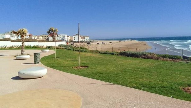 A coastal walkway with a beach, palm trees, and buildings in the background. - New And Furnished Apartment 5 Min From Beach On Foot (Agadir)