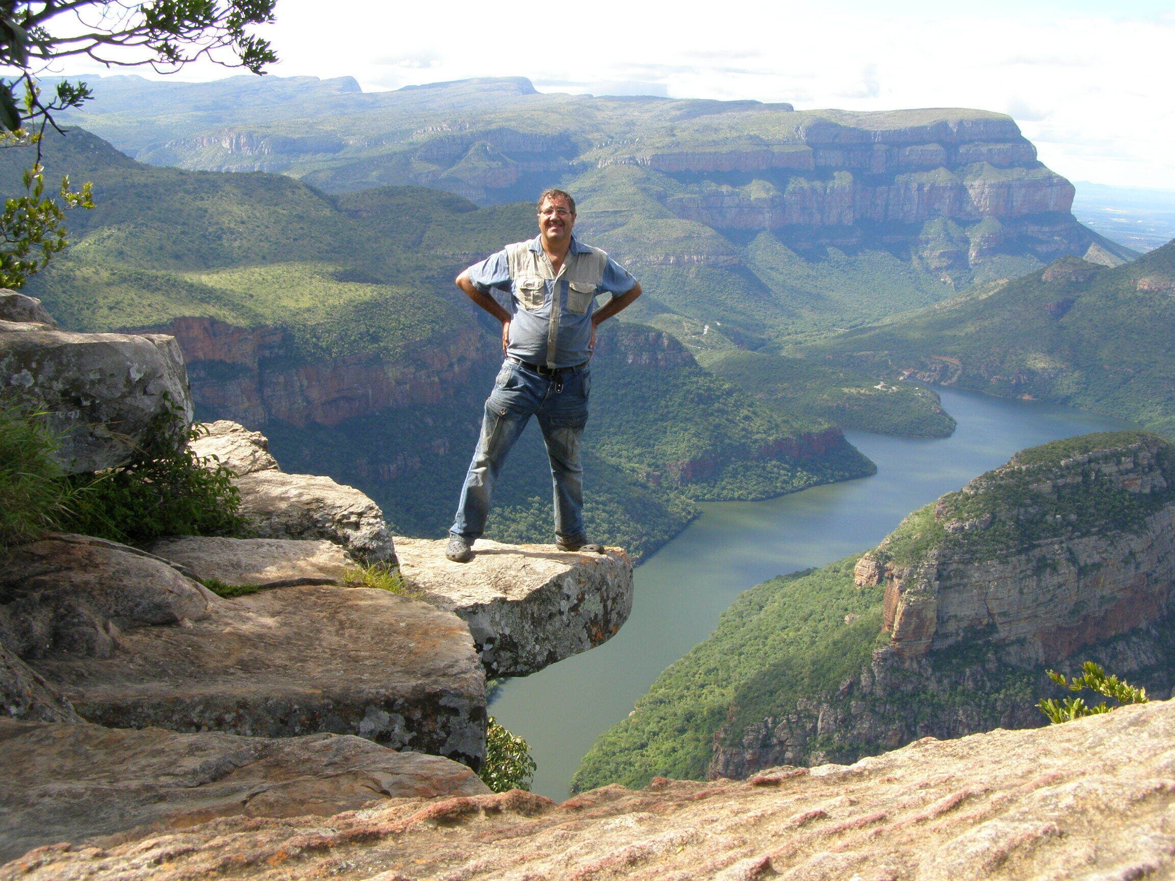 A person standing on a rock ledge overlooking a canyon with a river.