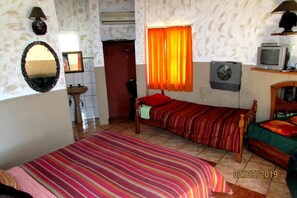 Una habitación pequeña y acogedora con cama, cómoda, espejo, ventana con cortinas, televisor y ventilador.
