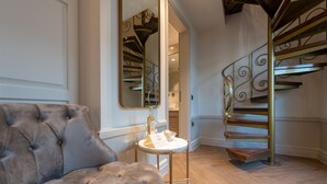 Un canapé capitonné, une petite table ronde avec une bouteille et une serviette, et un escalier en colimaçon avec des rampes en métal.