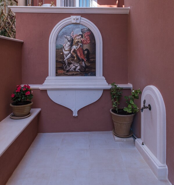Un pequeño patio con un mural, dos plantas en macetas y una puerta blanca.