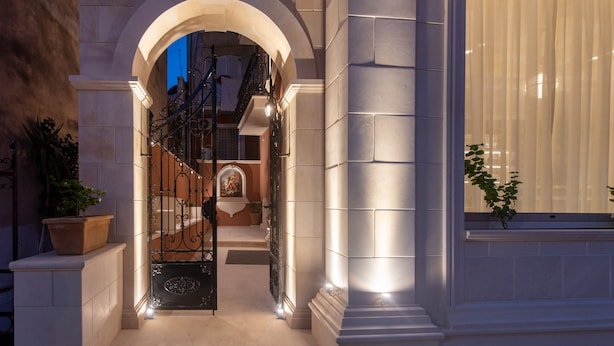 Une entrée imposante, agrémentée d’un portail en fer forgé, d’un escalier menant à un étage supérieur et d’une grande fenêtre ornée de rideaux légers.