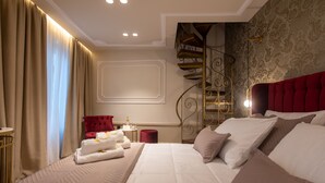 Une chambre d’hôtel avec un grand lit, une tête de lit rouge, une chaise rouge, une petite table avec une lampe et un escalier en colimaçon.