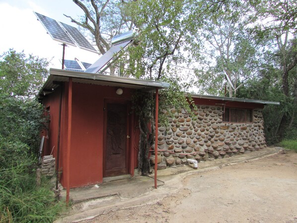 A rustic building with a red door and a stone wall, equipped with solar panels.