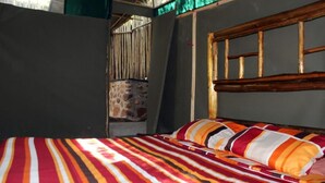 A bed with a striped bedspread and multiple pillows, a wooden headboard, and a stone wall in the background. - Two Bedroomed Bush-tent on the Klaserie River, With Free Lion Hyena Sounds (Hoedspruit)