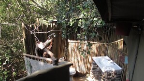 A rustic outdoor bathroom with a wooden fence, a stone wall, and a toilet. - 3 bed Bush-tent Under 3 Trees, for Couple Plus Chaperone Free Lionhyena Sounds (Hoedspruit)